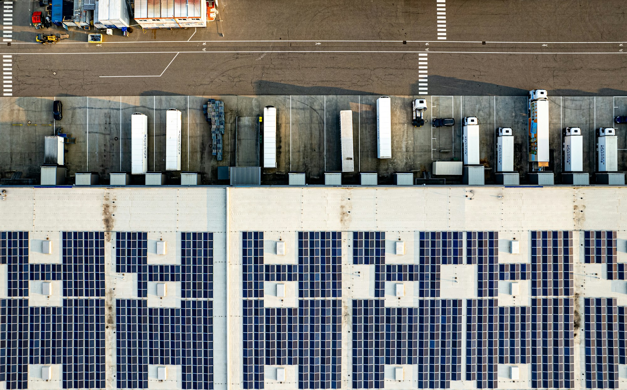 Luftaufnahme eines Logistikgebäudes mit Solarmodulen und Lkw an den Laderampen; Symbolfoto